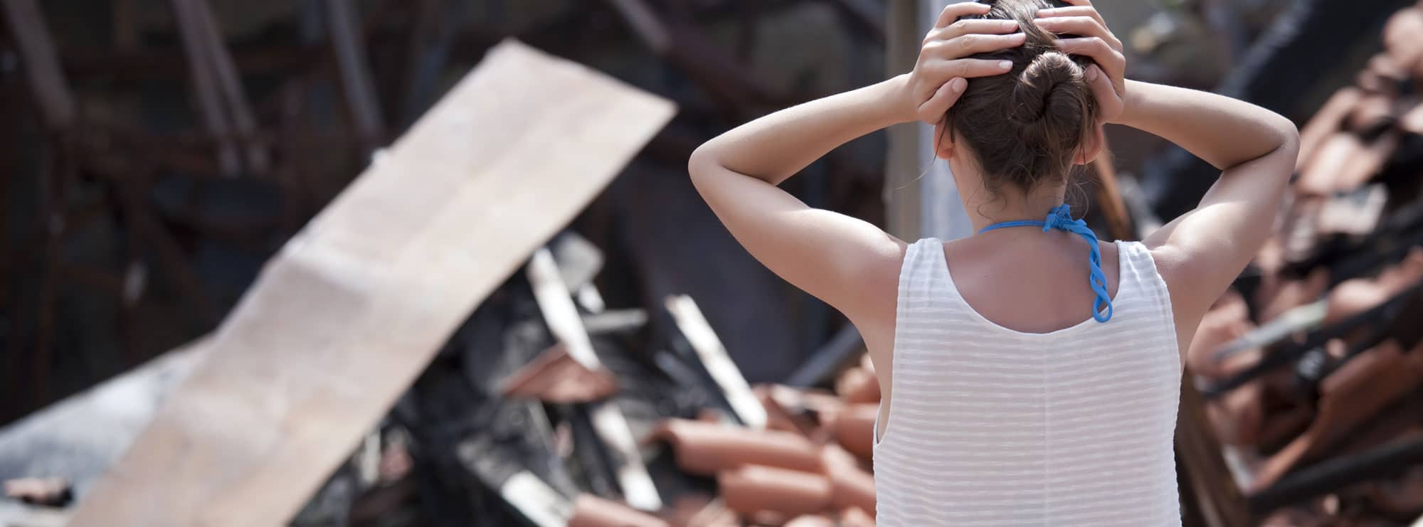 woman stands in front of burned house